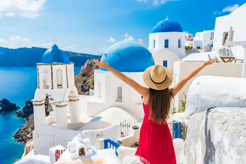 Woman with her hands in the air overlooking a landscape of white and blue houses on Santorini in Greece